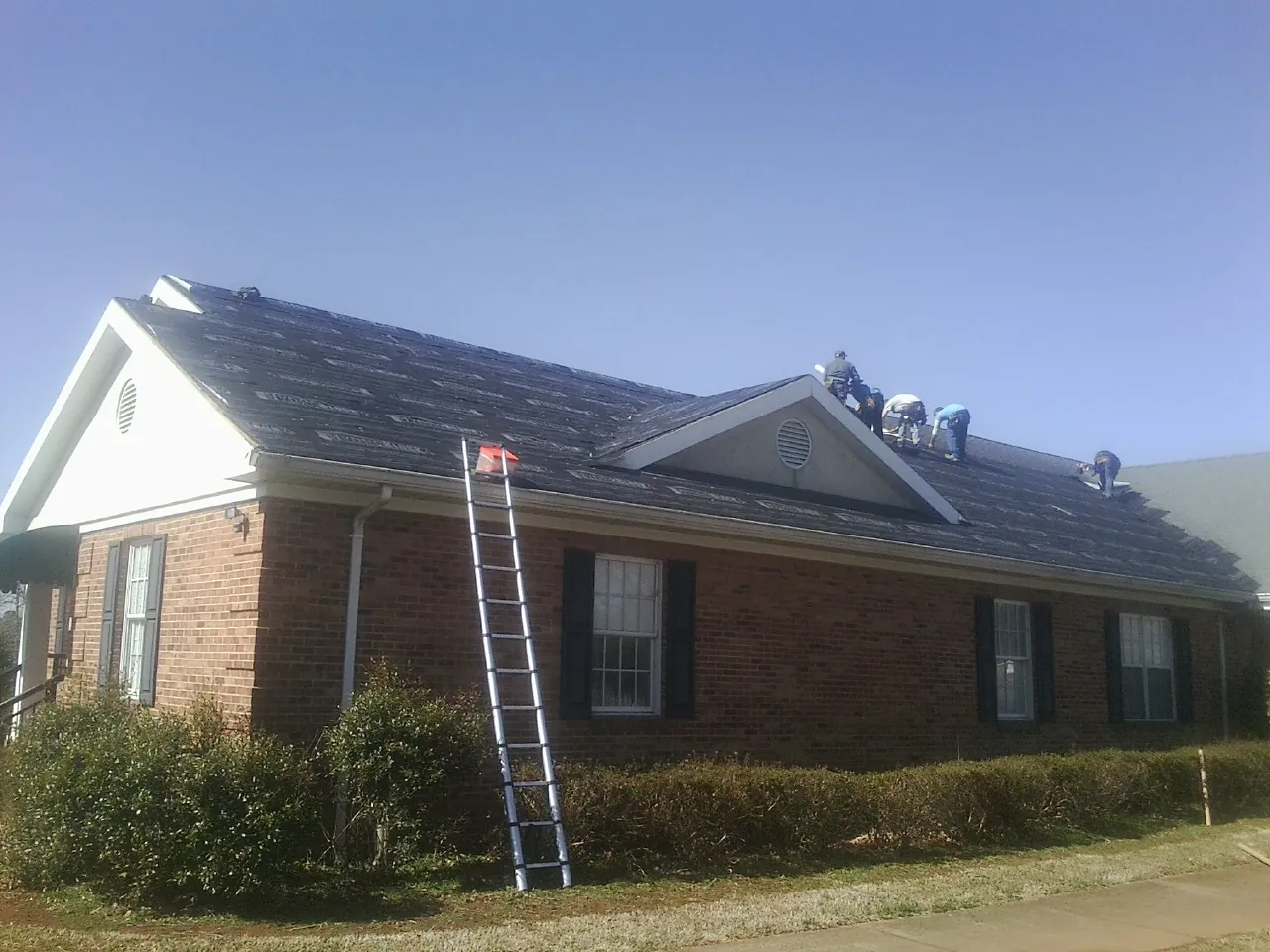 Crew tearing shingles off a brick ranch roof with a ladder set — Emergency Roof Repair work by our crew in Buhler
