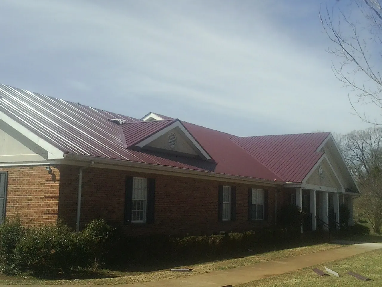 Red metal roof with gabled entries on a long brick building, from a Hail Damage Roof Repair job in Buhler
