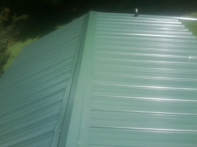 New green metal panels meeting at the ridge of a roof — Flat Roof Repair work by our crew in Buhler