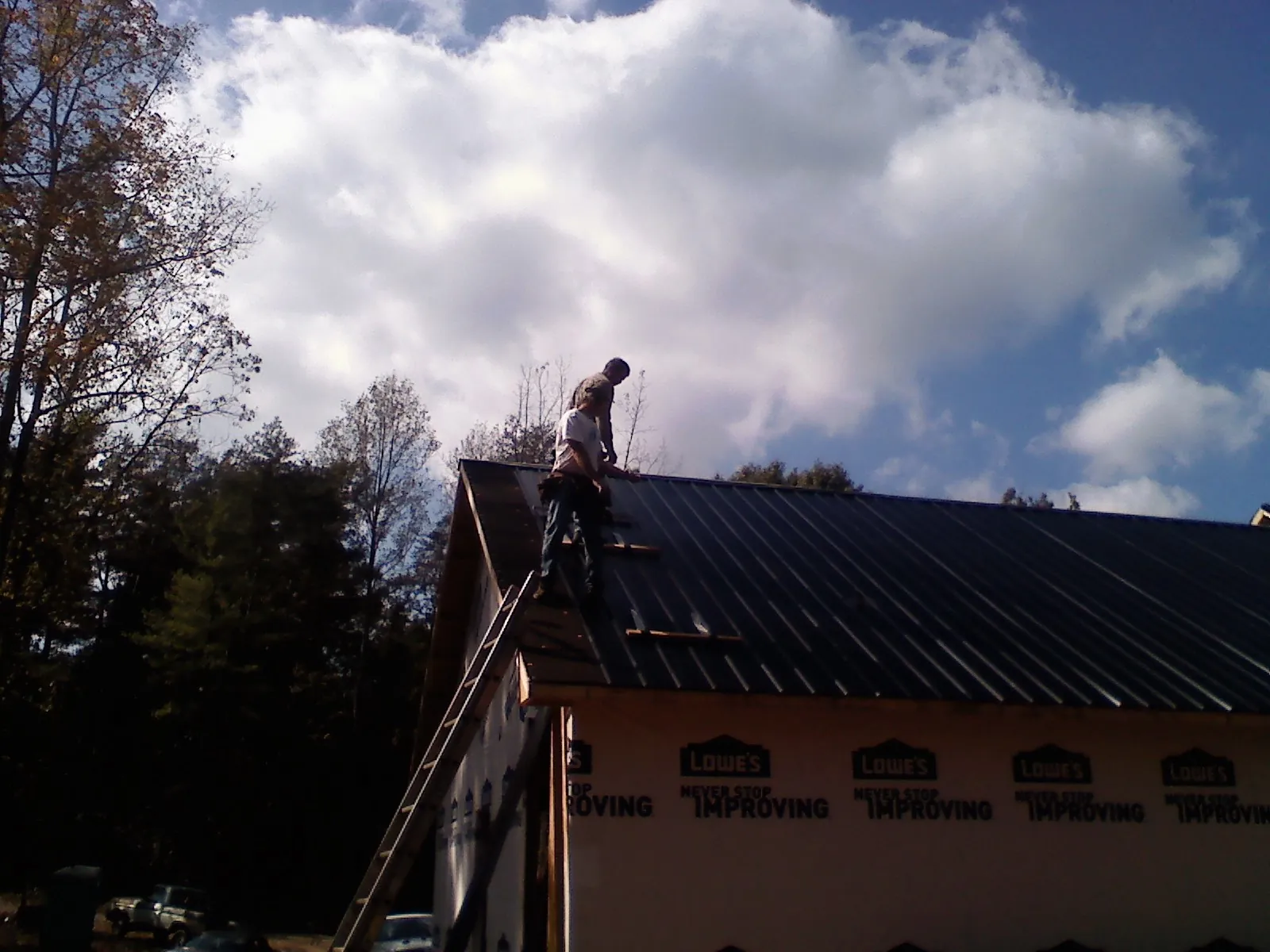 Roofer fastening dark metal panels high against a cloudy sky, from a Roof Inspection job in Buhler
