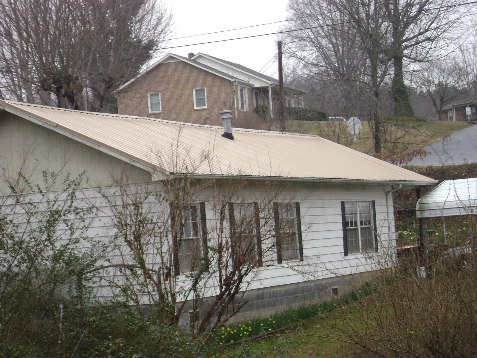 Tan metal roof on a white sided house set into a hillside — Commercial Roofing by Roofing Brothers in Buhler